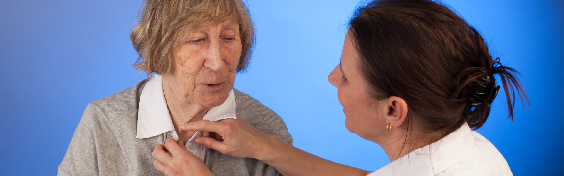 aide helping the senior woman on her shirt